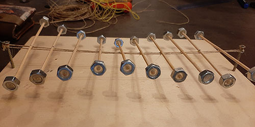Na slici se nalaze drveni štapići u nizu zaljepljeni na vodoravan dugački drveni štap. Na krajevima štapića nalaze se matice.