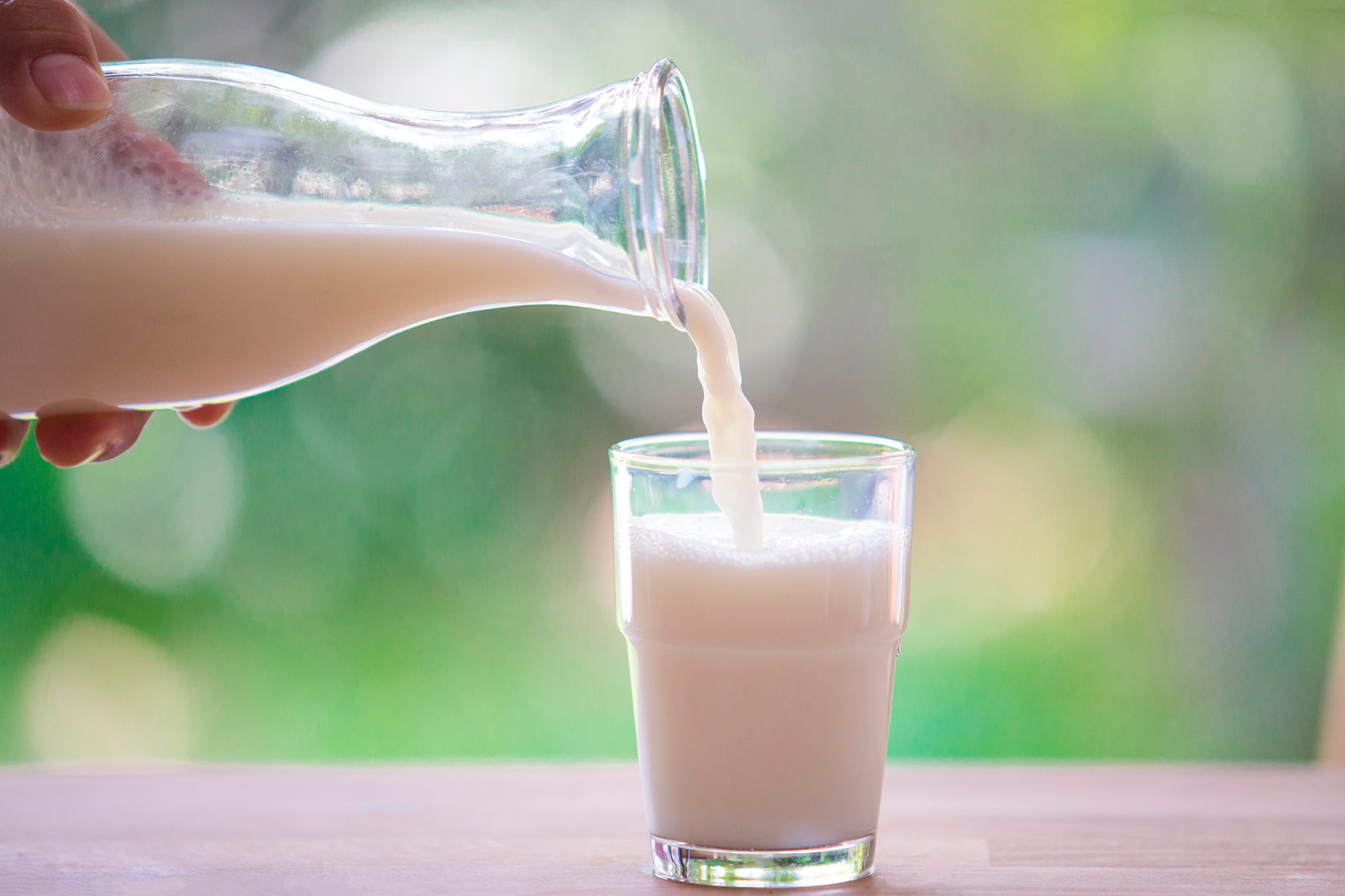 Fotografija prikazuje ruku osobe koja ulijeva mlijeko iz staklene boce u čašu.