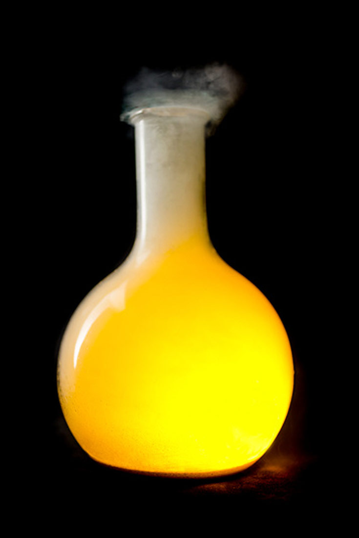 Fotografija prikazuje okruglu tikvicu s ravnim dnom. U tikvici se vidi reakcija natrija i klora, primjećuje se žuto svjetlo, na vrhu tikvice izlazi bijeli dim