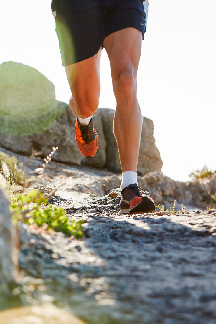 Fotografija prikazuje noge muškog trkača koji trči po stjenovitoj stazi. U pozadini se vide obrisi gorja.