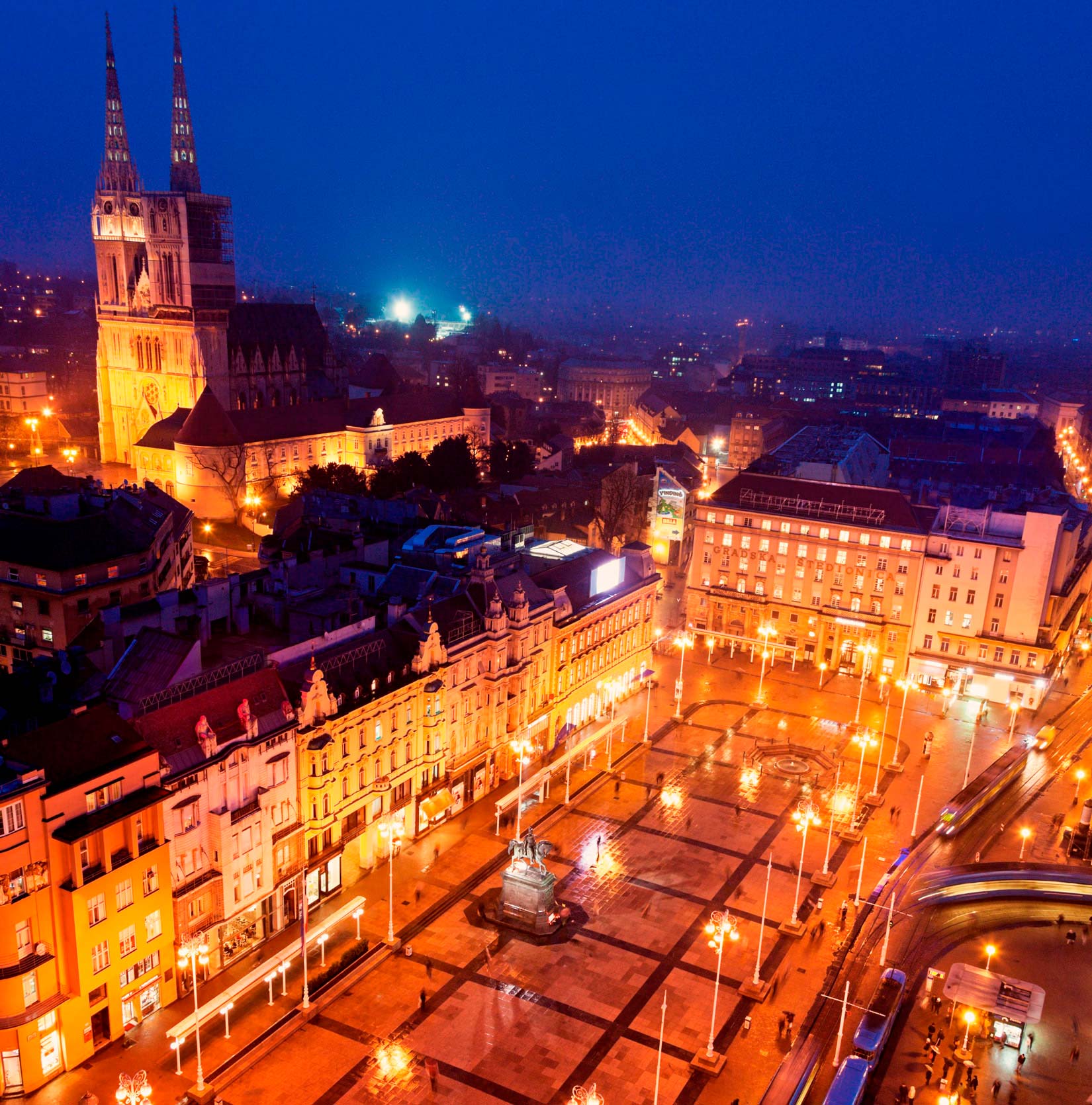 Fotografija prikazuje pogled iz zraka na Trg bana Josipa Jelačića u Zagrebu. Trg je obasjan noćnom rasvjetom.