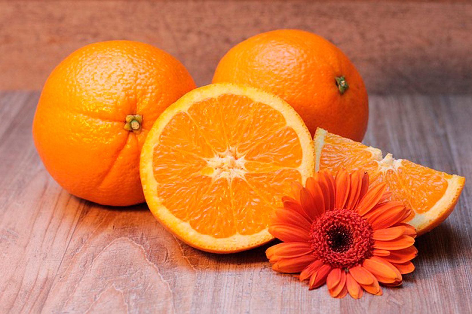 Na slici su dvije cijele neoguljene naranče, jedna prerezana na pola te još jedna četvrtina.