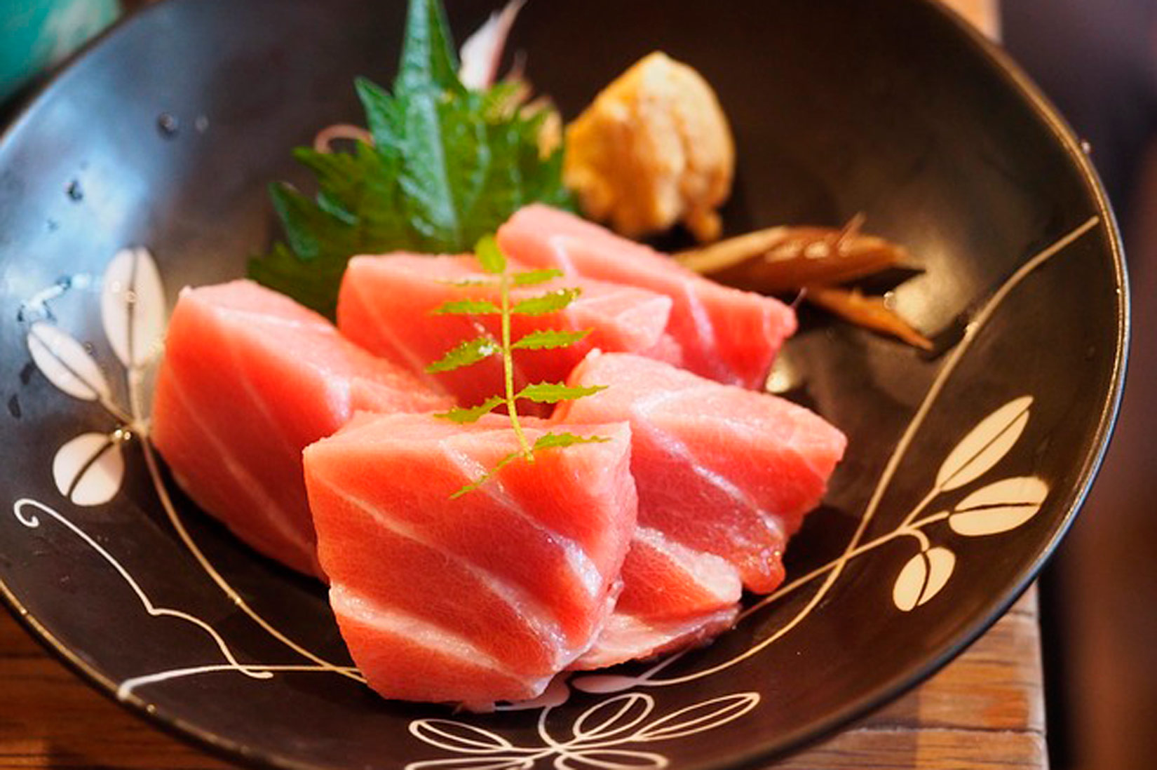 na slici se vidi tuna narezana na kocke, pet komada, poslužena u crnom tanjuru s bijelim motivom lišća.