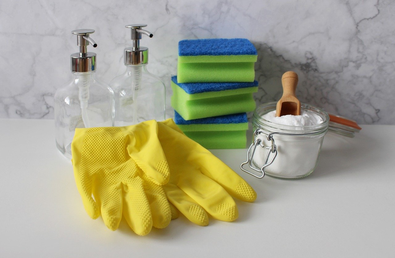 Slikom je prikazan dio kupaonice na kojem stoje rukavice za čišćenje, spužve, prazne boce sapuna i sredstvo za čišćenje.