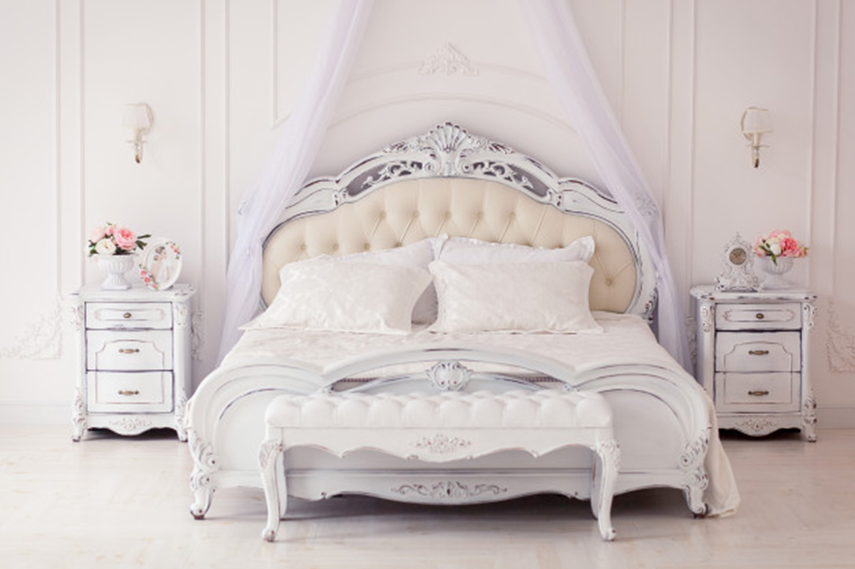 Slikom je prikazana spavaća soba u kojoj je bijeli krevet, dva bijela noćna ormarića i na njima cvijeće.