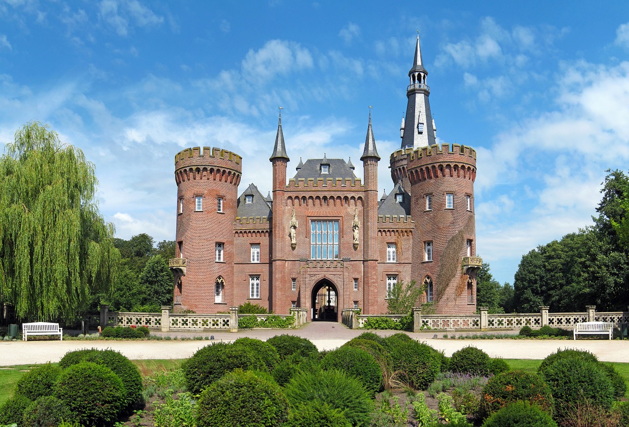 Slikom je prikazan dvorac s visokim tornjevima i zelenim okolišem.