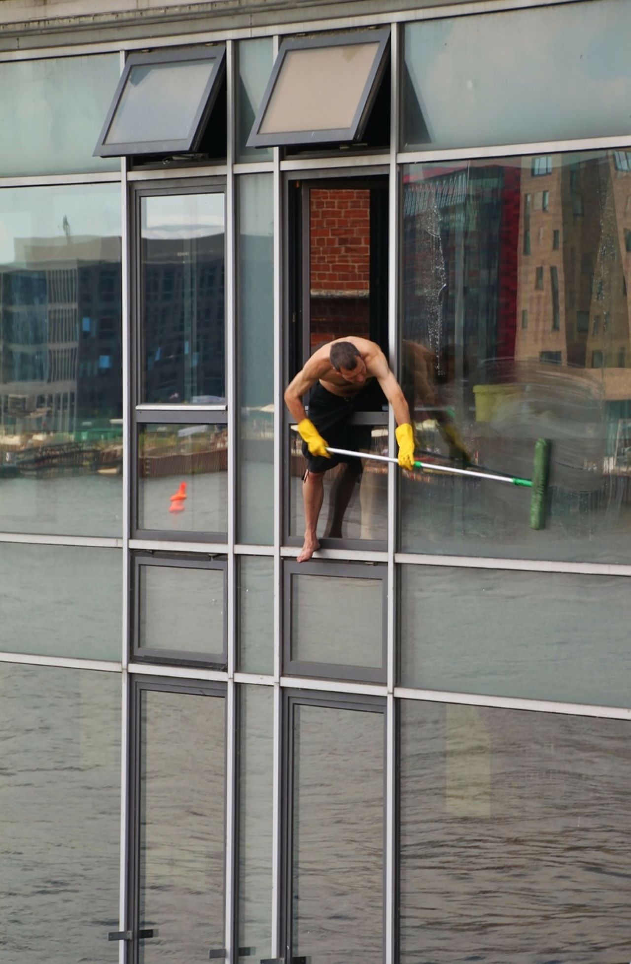 Slikom je prikazan čovjek koji pere prozore visoke zgrade.