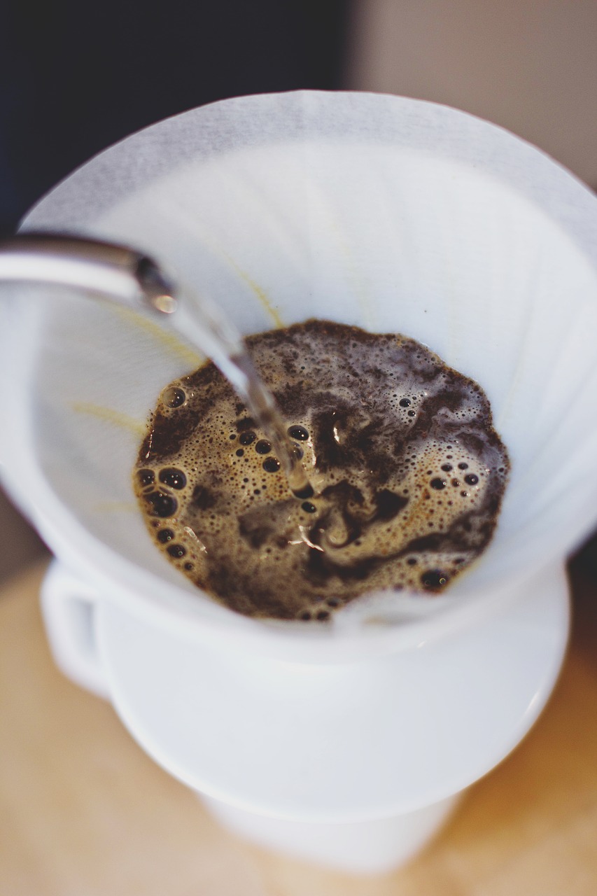 Na slici se vidi (odozgo) bijela šalica u kojoj je filtrirana kava . Iz tanke cijevi aparta curi voda.
