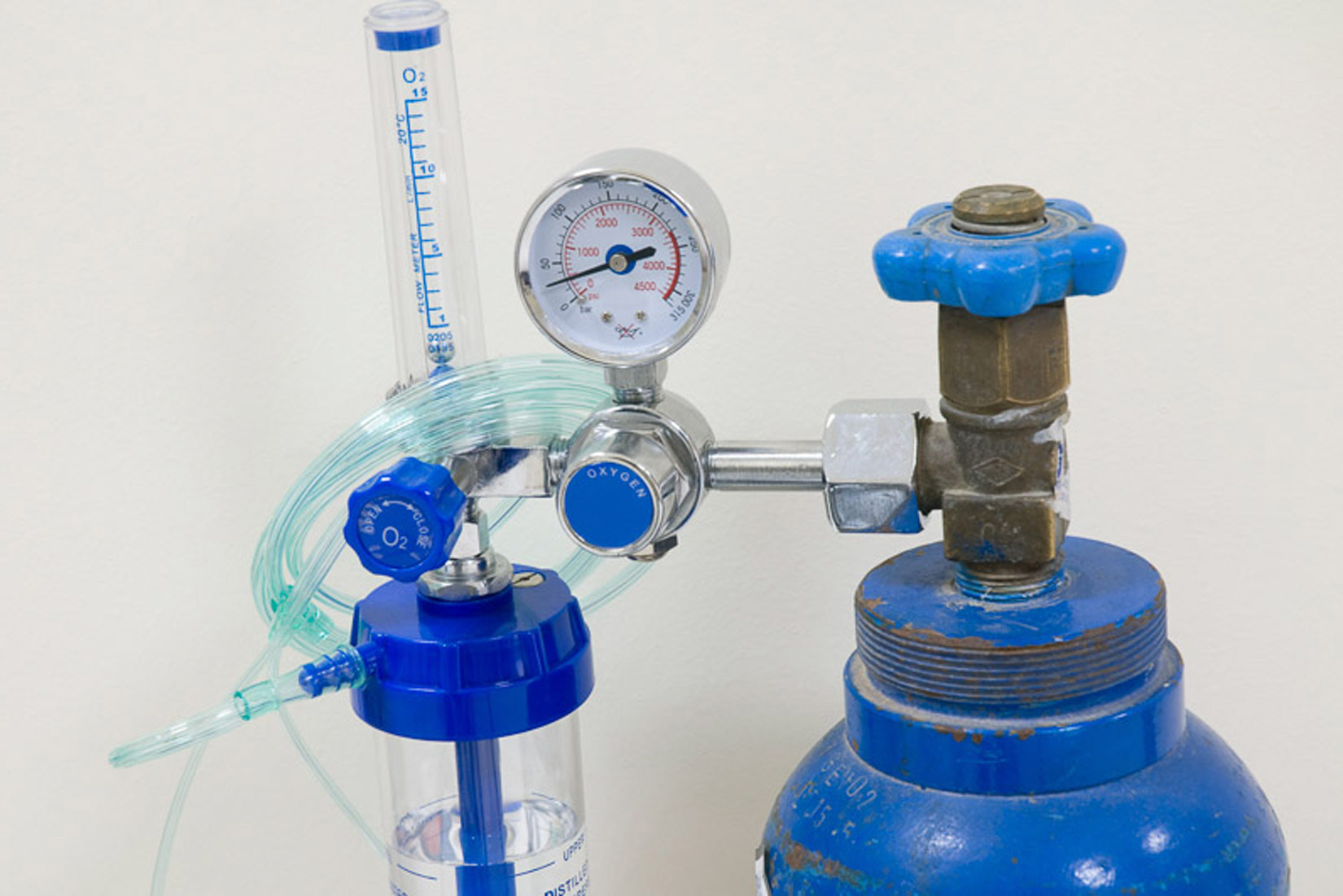Na fotografiji je prikazan vrh plave čelične boce u kojoj se čuva kisik. Na vrhu boce je ventil, a sama boca je spojena na sustav koji pokazuje vrijednost tlaka.