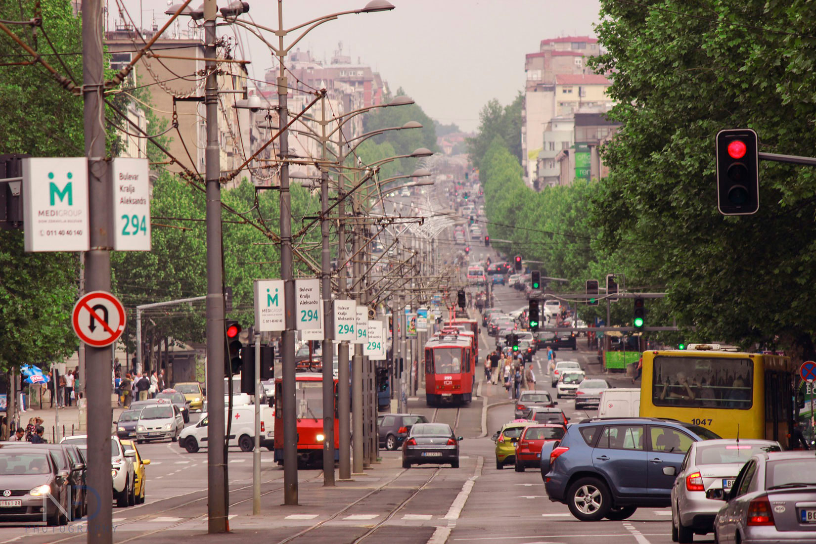 Na slici je prikazana prometna ulica.Ispušni plinovi automobila u gradovima uzrokuju smog. Na njoj se vide pješaci, mnoštvo automobila, tramvaji i autobus.