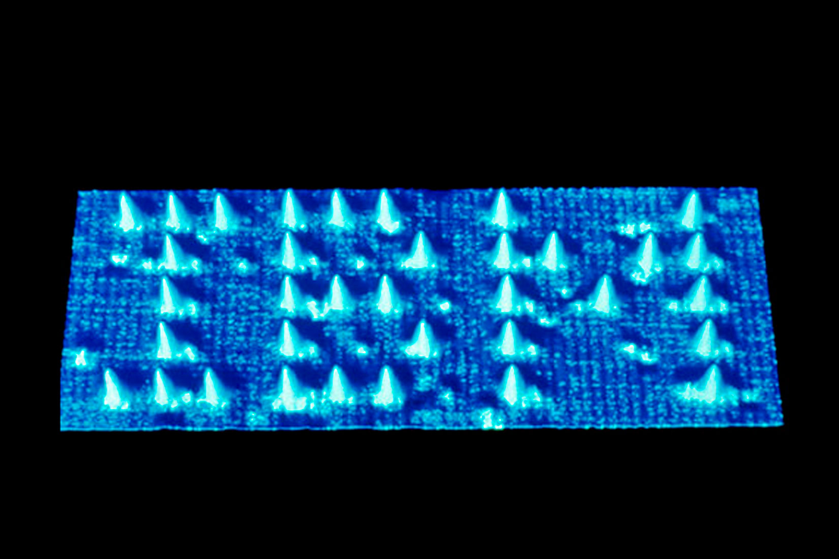 Slika prikazuje plavu pravokutnu ploču na kojoj ispupčenim čunjićima piše IBM. To je uvećani prikaz koji se može vidjeti elektronskim mikroskopom.