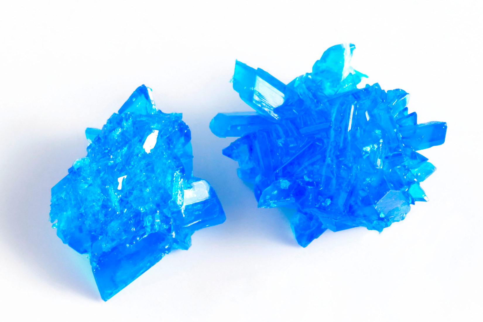 Fotografija prikazuje dva grumena modre galice. Vrlo su nepravlina oblika i oštro nazubljeni.