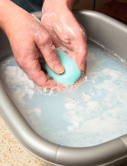 Fotografija prikazuje pranje sapunom u posudi napunjenoj vodom. Sapun je u rukama neke osobe, a površina vode je zapjenjena.