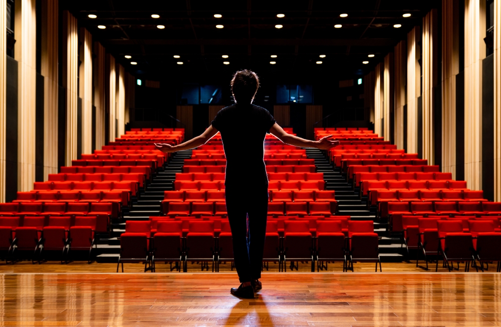 Na ovoj je slici prikazan muškarac koji stoji na pozornici okrenut prema praznom gledalištu.