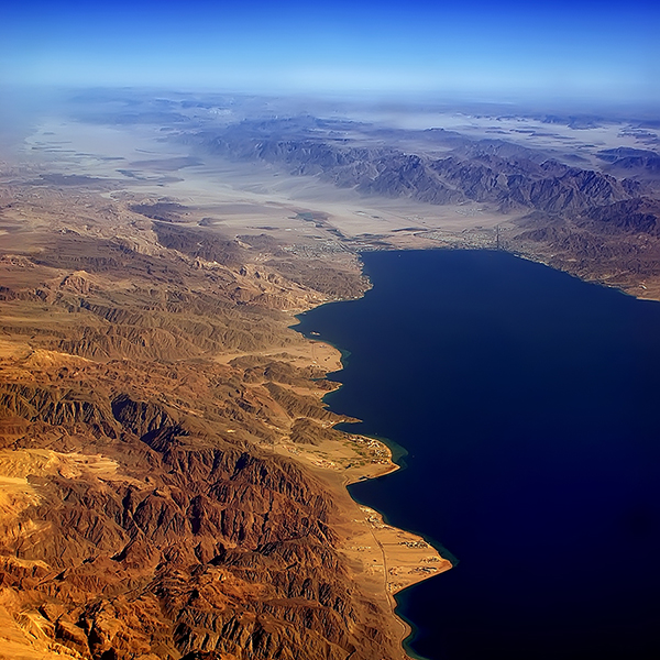 Fotografija prikazuje tamno-modri morski zaljev kako naizgled prodire u smeđi pustinjski krajolik prošaran ogoljenim brdima