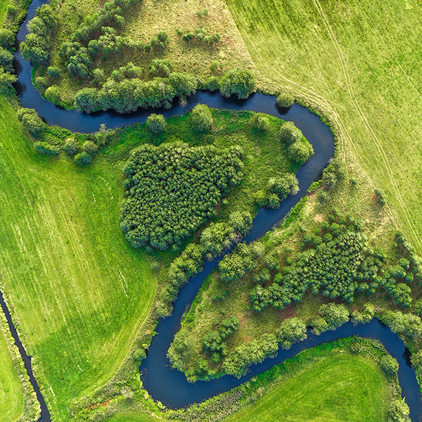 Fotografija prikazuje plavu, usku rijeku koja nalikuje na zmiju koja teče kroz svjetlo zelenu ravnicu, koja djeluje veoma svježe zbog svog bujnog travnatog pokrova