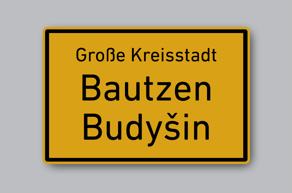 Slika prikazuje cestovnu oznaku mjesta na njemačkome i jeziku Lužičkih Srba: Bauzen / Budyšin.
