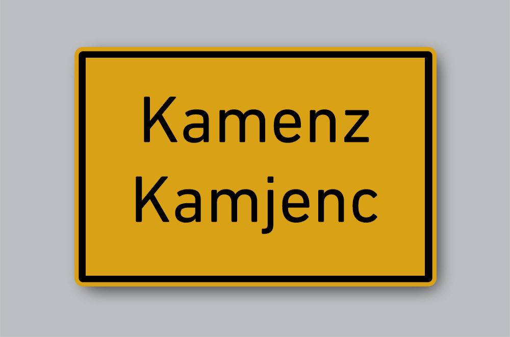 Slika prikazuje cestovnu oznaku mjesta na njemačkome i jeziku Lužičkih Srba: Kamenz / Kamjenz.