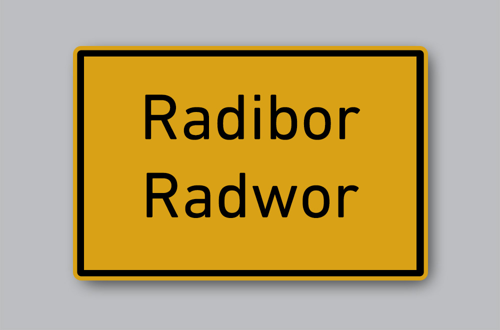 Slika prikazuje cestovnu oznaku mjesta na njemačkome i jeziku Lužičkih Srba: Radibor / Radwor.