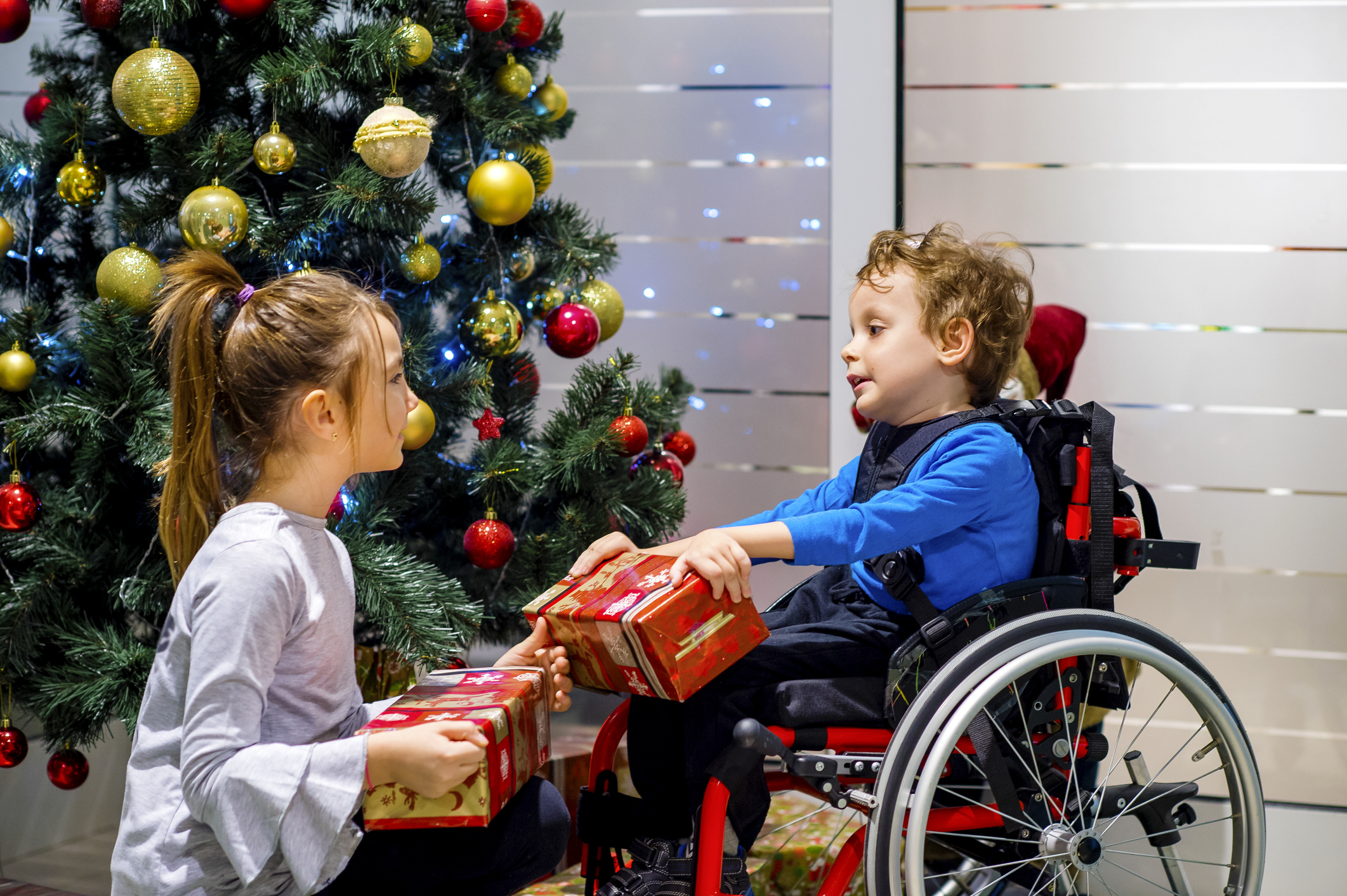 Djevojčica predaje darove dječačiću u invalidskim kolicima.
