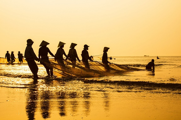 Fotografija prikazuje ribare koji iz mora izvlače mrežu.