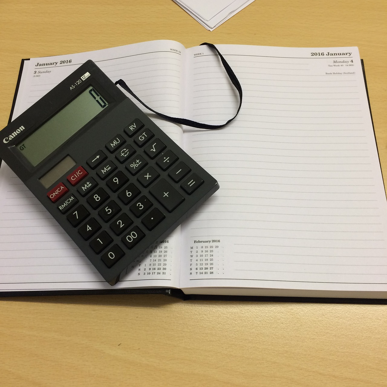 Fotografija prikazuje otvorenu bilježnicu na kojoj se nalazi džepni kalkulator.
