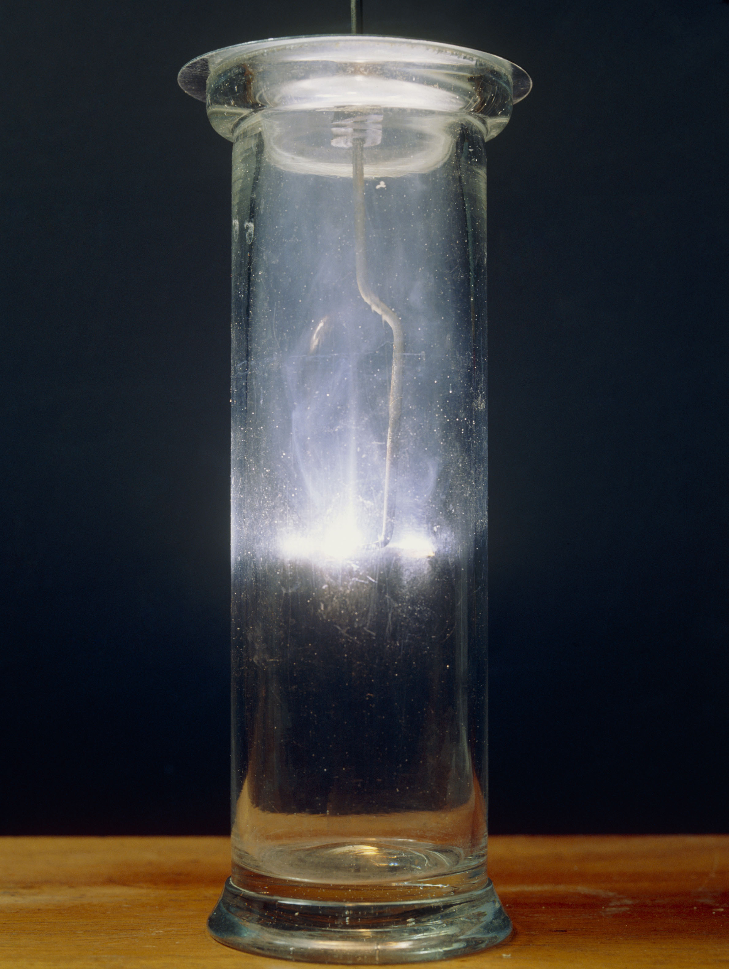 Fotografija prikazuje valjkastu, staklenu, prozirnu posudu u kojoj se događa reakcija gorenja kalcija