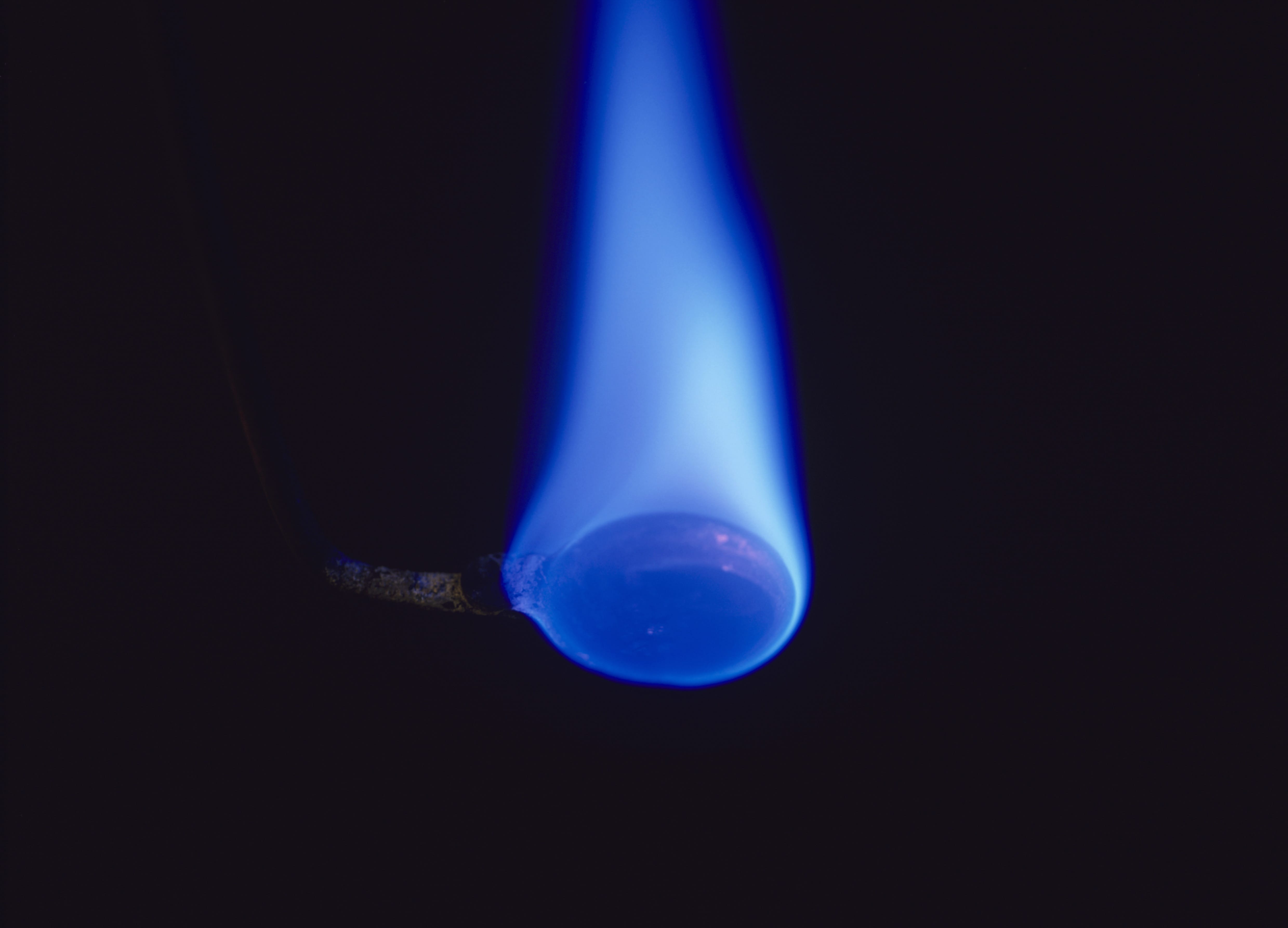 Fotografija prikazuje gorenje sumpora. Pozadina je crna, a plamen plave boje.