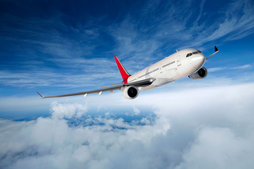 Fotografija prikazuje avion u letu.Avion je bijele i crvene boje; Nebo je plavo i vide se bijeli oblaci.