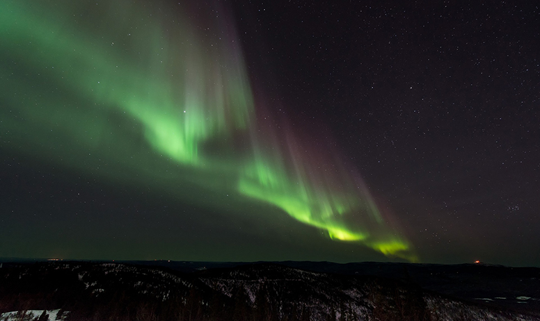Fotografija prikazuje polarno svjetlo na noćnom nebu, fluorescentno zelene boje.
